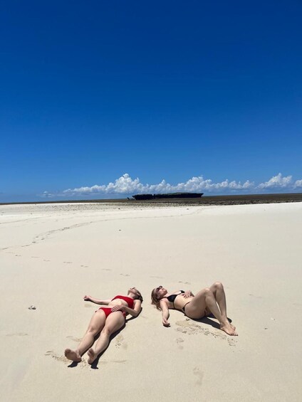 Two people lying on a sandy beach with a clear sky and a ship in the distance. 5