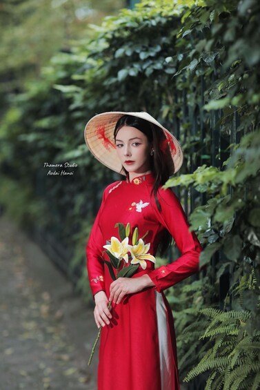 A person in a red dress holding a flower, standing by a path with greenery. 3