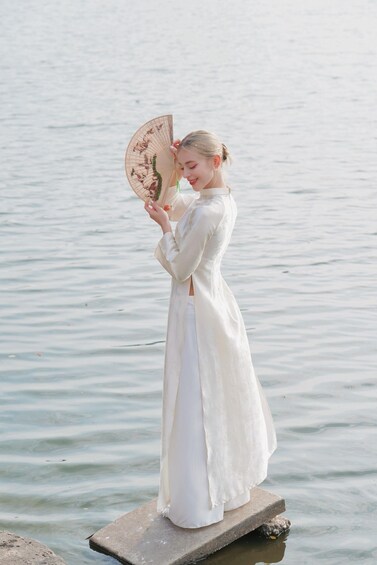 A person in a white dress standing on a platform by a calm body of water. 5