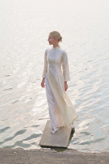 A person in a white dress standing on a concrete platform by a body of water. 4