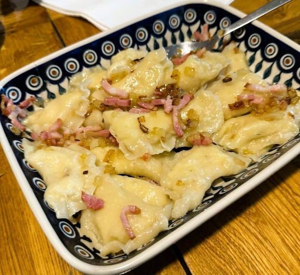 A plate of dumplings with a creamy sauce, garnished with bits of ham and onions. 3