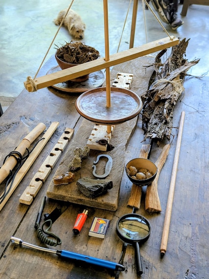 A wooden table with various tools, a balance scale, and a dog in the background. 4