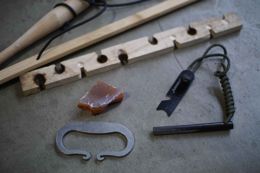 A wooden tool with holes, a metal hook, a metal piece with a curved top, and a green cord. 1