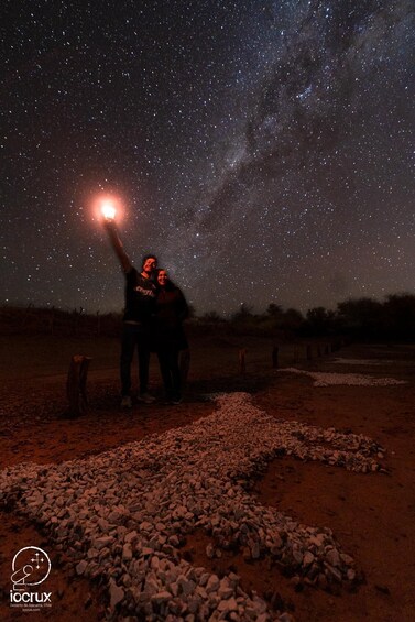 Two people standing on a rocky ground under a starry night sky. 1