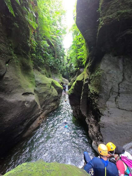 A narrow water channel flanked by moss-covered rocks, with rafters navigating the passage. 1