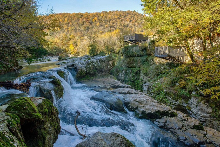 A cascading river, a wooden viewing platform, and a forested hillside. 1
