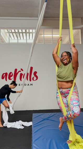 A person performing aerial silk acrobatics in a studio with a backdrop that reads 'aertrils'. 4