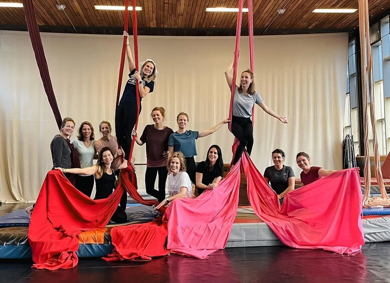 A group of people engaged in aerial silk acrobatics in an indoor studio with wooden ceilings and large windows. 1