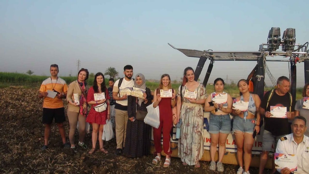 A group of people standing in a field with a large piece of machinery in the background. 4