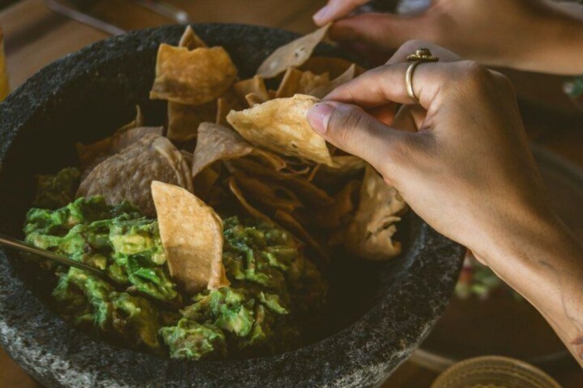 A person serving guacamole with tortilla chips from a stone bowl. 2