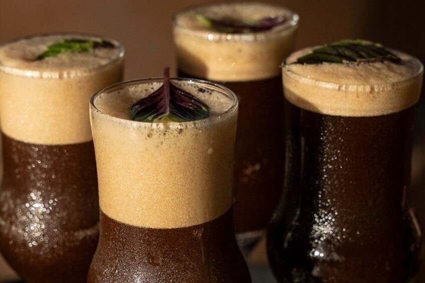 Four glasses of a dark beverage with a frothy top, possibly a cocktail, with a garnish on one. 3