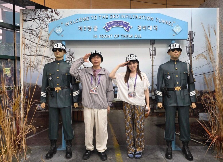 Four individuals in military uniforms standing in front of a sign that reads 'WELCOME TO THE 3RD INFILTRATION TUNNEL IN FRONT OF THEM ALL.' 4
