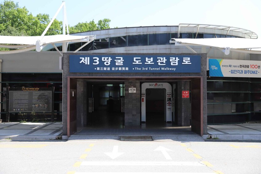 A building entrance with a sign for 'The 3rd Tunnel Walkway' and a contact number. 3