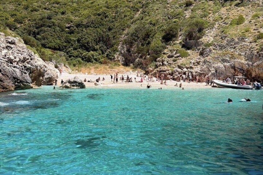 A coastal beach with clear turquoise water, rocky cliffs, and a boat on the shore. 5