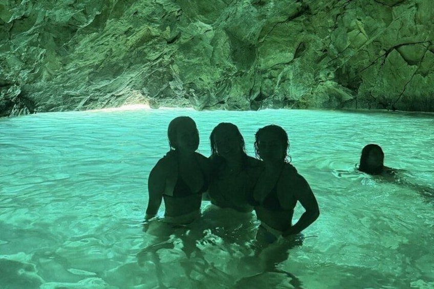Three people in a turquoise pool surrounded by rocky cave walls. 4