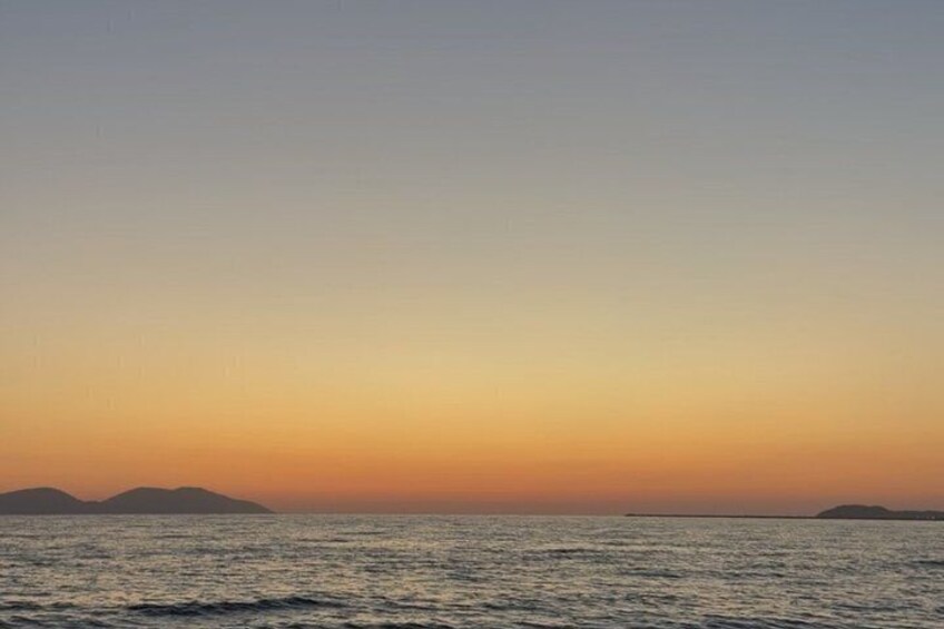 A sunset over a calm sea with distant landforms. 2