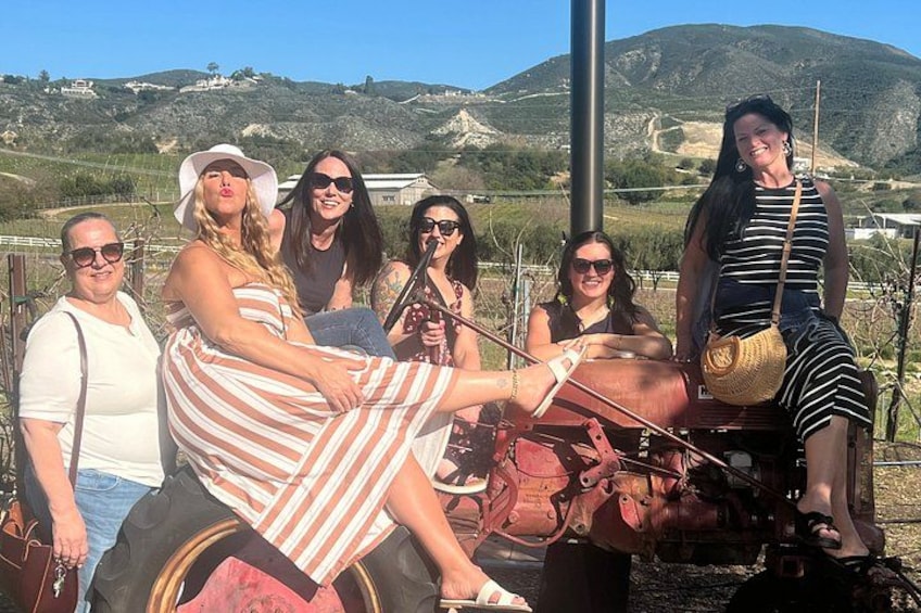 A group of people posing with a vintage tractor in a rural landscape with hills in the background. 4