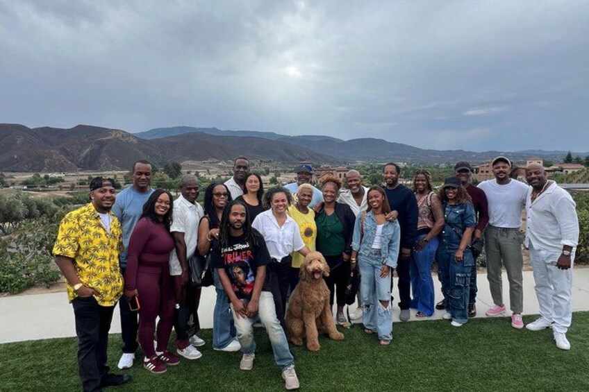 A group of people posing on a grassy area with a mountainous landscape in the background. 2