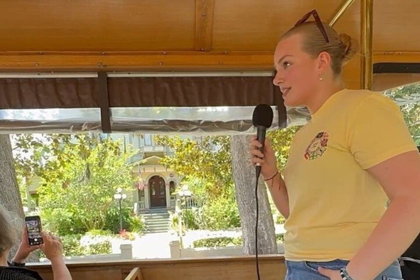 A person holding a microphone, standing in a wooden structure with a view of a building and trees. 3