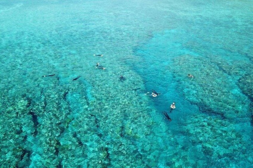 An aerial view of a clear blue sea with visible coral reefs and snorkelers. 3