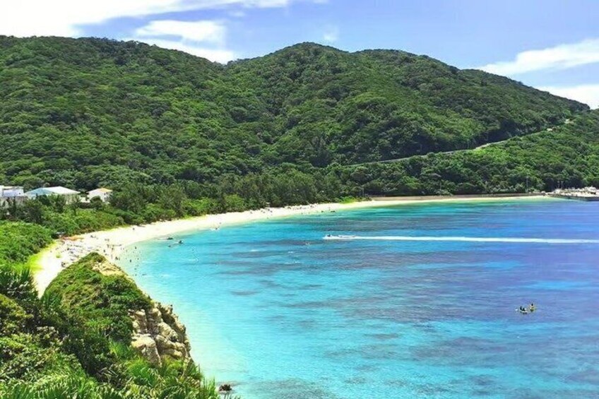 A coastal landscape with a beach, clear turquoise waters, and a forested hill in the background. 3