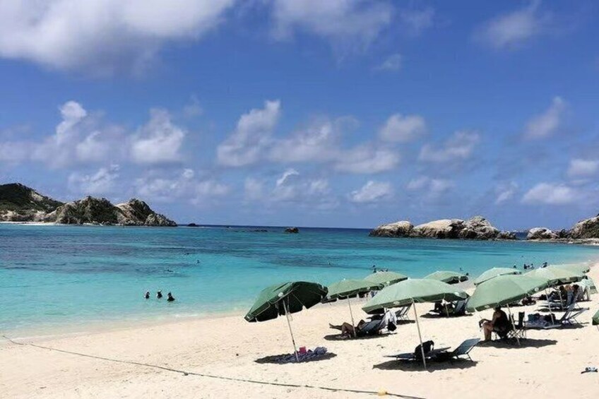 A beach with clear turquoise water, people swimming, and umbrellas on the sand. 2