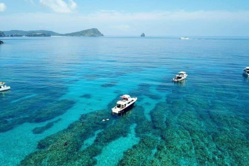 A clear blue sea with boats and a distant island. 2