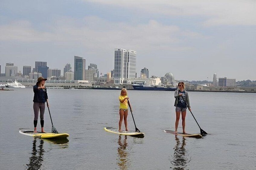 Three people paddleboarding on a calm body of water with a city skyline in the background. 4