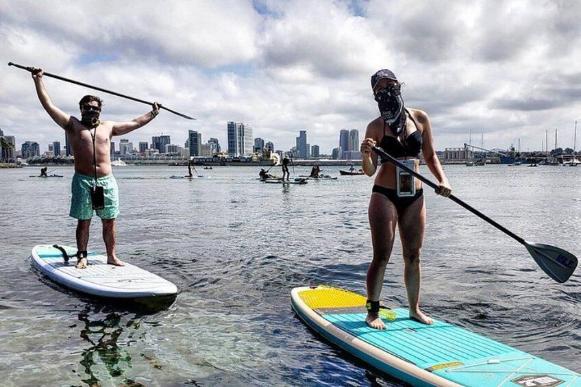 Two people paddleboarding on a body of water with a city skyline in the background. 5