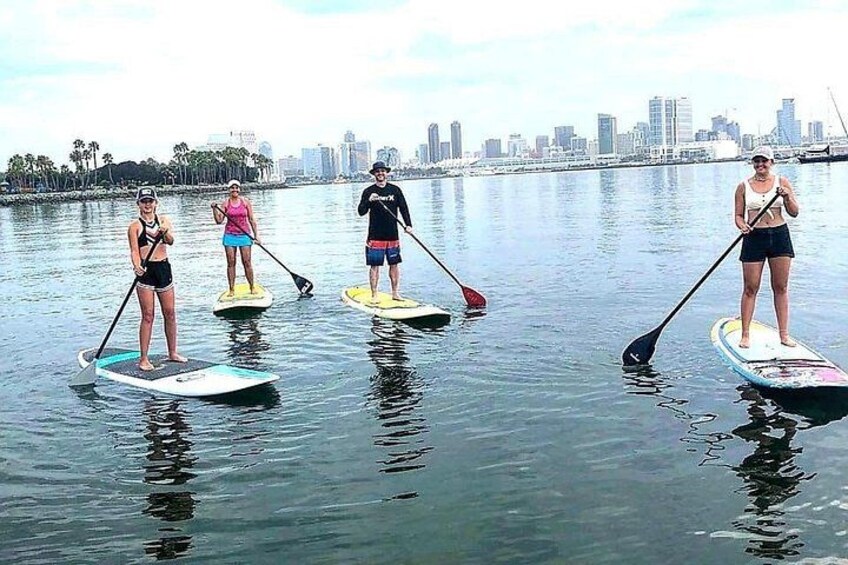 People paddleboarding on calm water with a city skyline in the background. 4