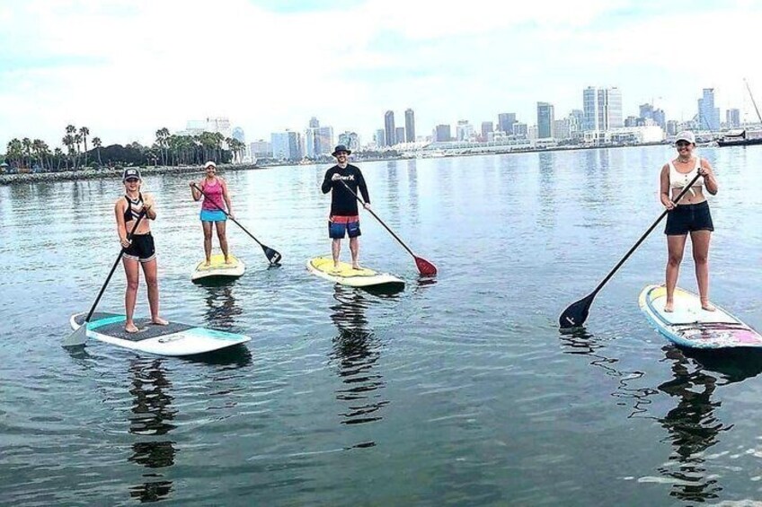 People paddleboarding on calm water with a city skyline in the background. 4