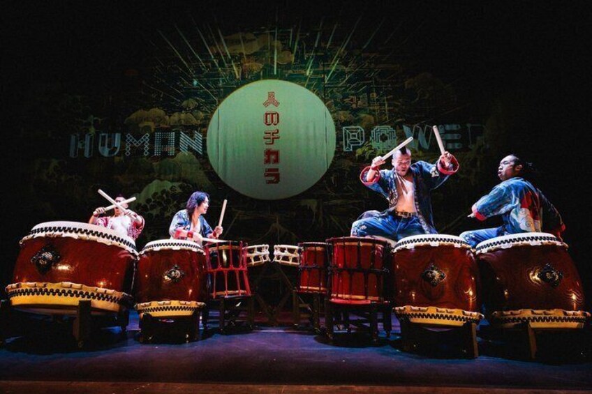 A drum performance with performers on large drums, a large green ball, and a backdrop with 'HUMMUN' text. 2