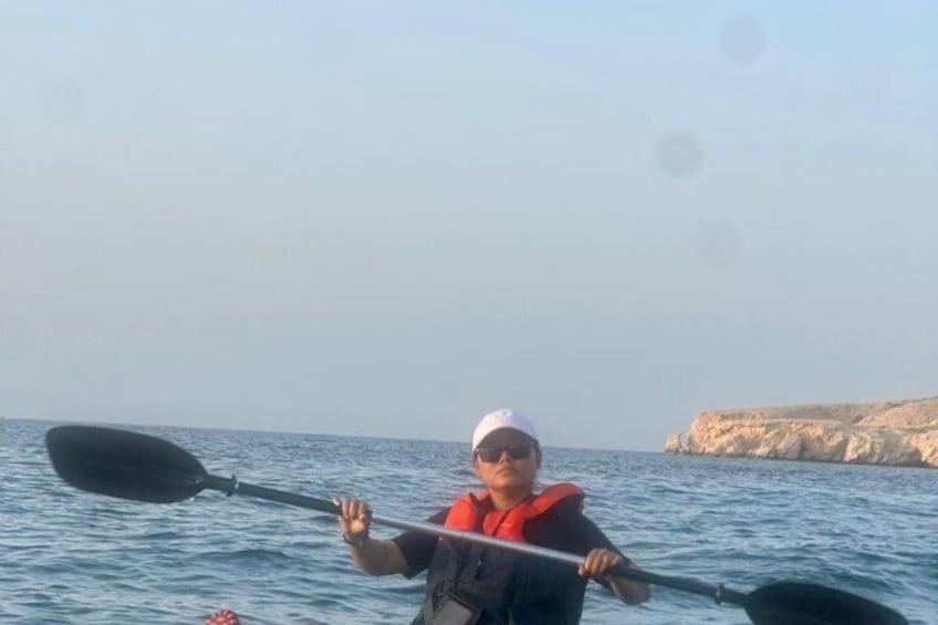 A person kayaking on calm water with a rocky coastline in the background. 1