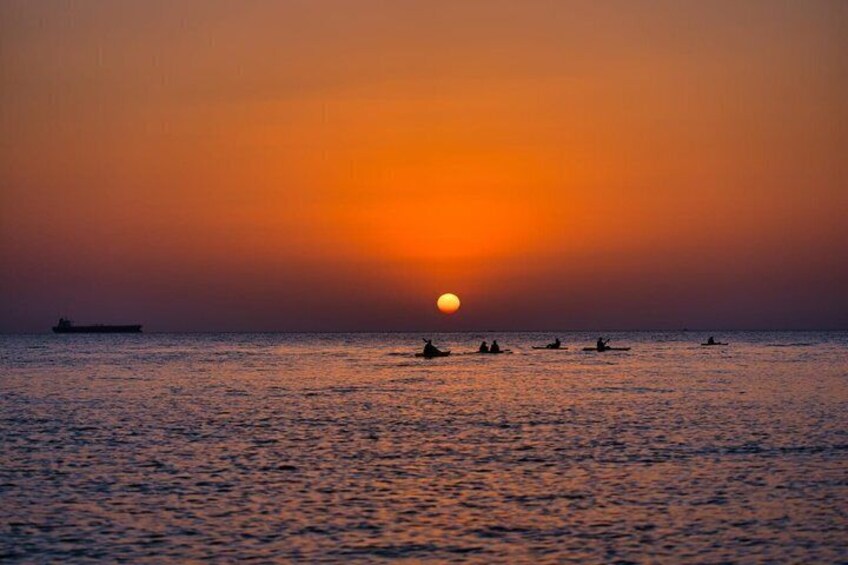 A sunset over the ocean with a ship and several boats. 3