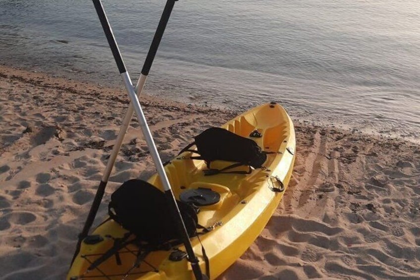 A yellow kayak on a sandy beach with a fishing rod leaning against it. 2