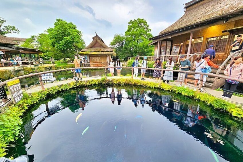 A traditional wooden building with a thatched roof, surrounded by a pond with reflections and a wooden fence. 2