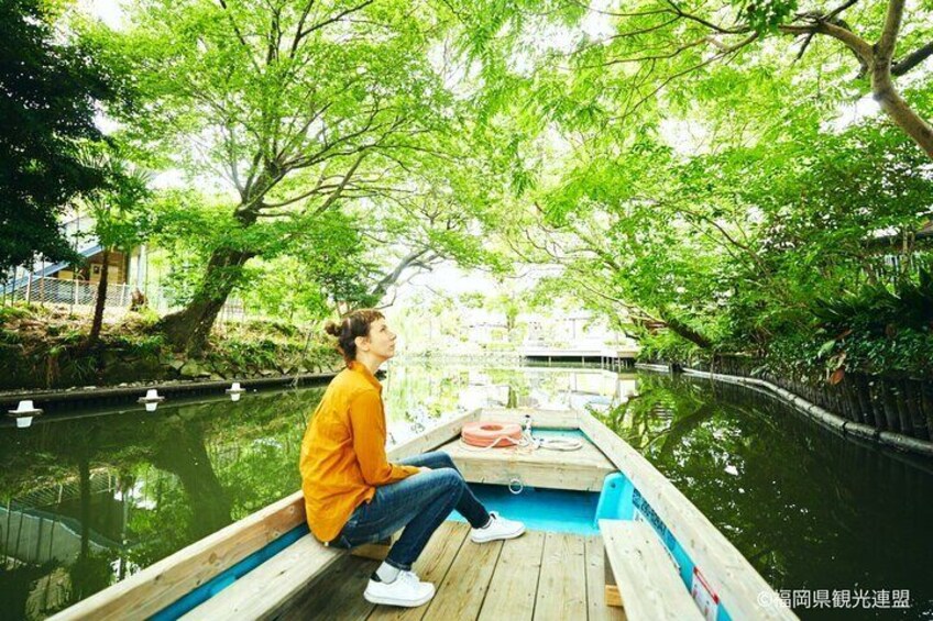 A person sitting on a wooden boat in a canal surrounded by trees. 5