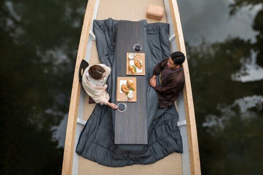 Two people on a narrow boat with a table set for a meal. 2