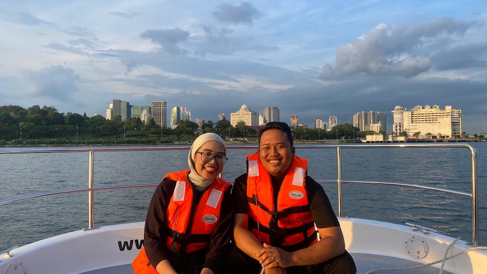 Two people on a boat wearing life jackets, with a city skyline in the background. 2