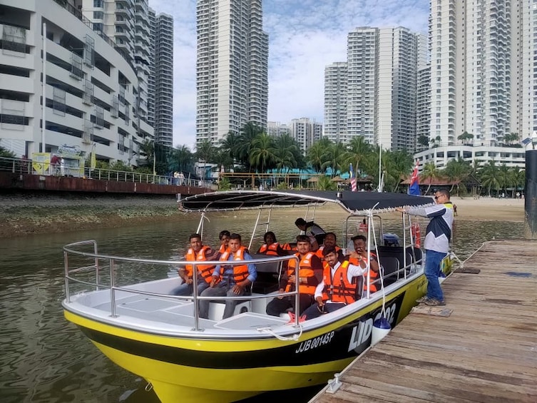 A boat with passengers wearing life jackets docked at a pier with high-rise buildings in the background. 1