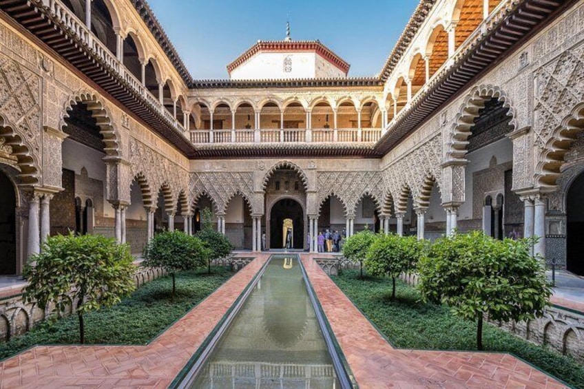 A courtyard with a central water channel, surrounded by arches and greenery. 1