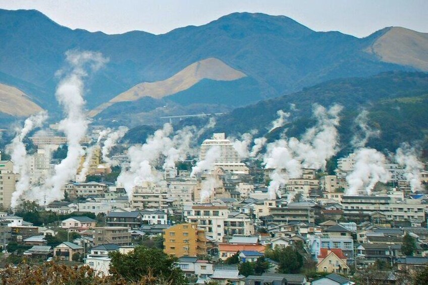 A cityscape with numerous buildings emitting smoke, surrounded by mountains. 2