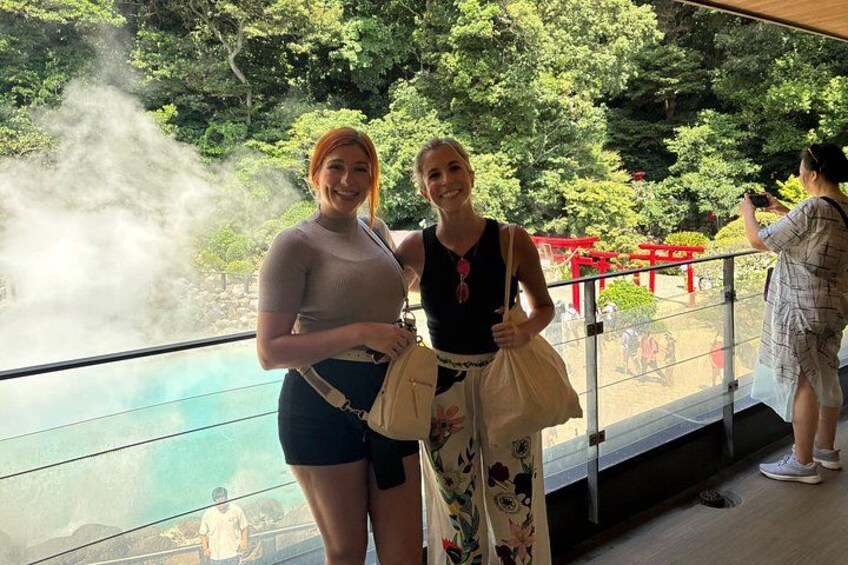 Two people standing by a glass railing with a view of a traditional Japanese torii gate and greenery in the background. 2