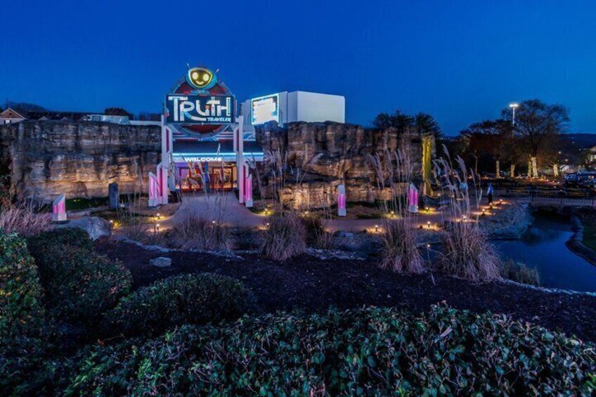 A nighttime view of a themed entrance with a sign reading 'Truth Teller' and a neon-lit pathway leading to it. 4
