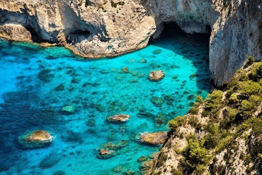 A coastal landscape with clear turquoise waters, rocky formations, and sparse vegetation. 5