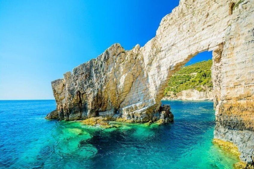 A coastal rock formation with a natural arch over clear blue waters. 3