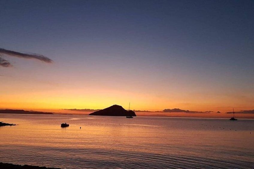A calm body of water at sunset with a small island and a sailboat. 5