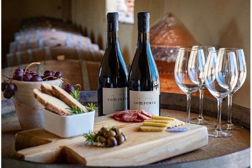 A wooden table with wine bottles, glasses, grapes, bread, and cheese. 3