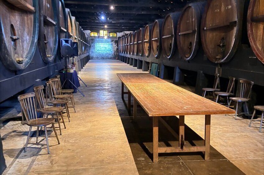 A wine cellar with wooden barrels, a long table, and chairs. 2