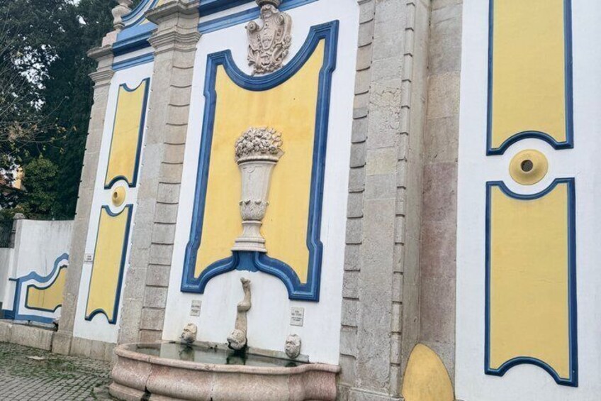 A fountain with a decorative urn, surrounded by a wall with blue and yellow trim. 4